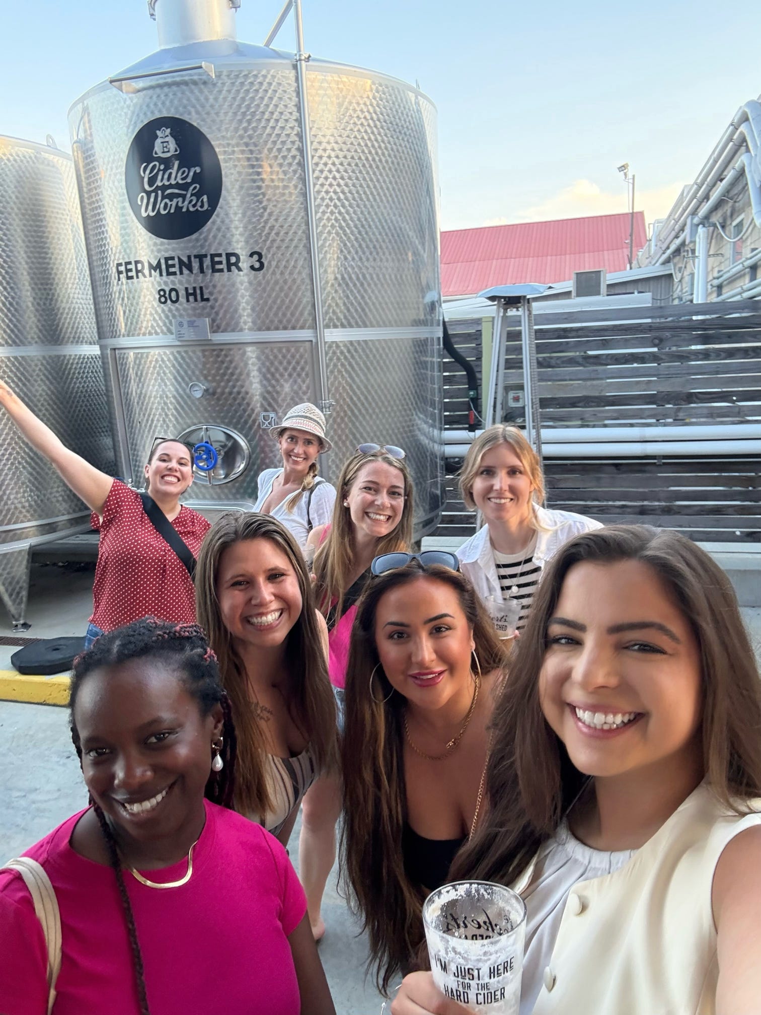 Group of people posing for a selfie in front of a cider works fermenter