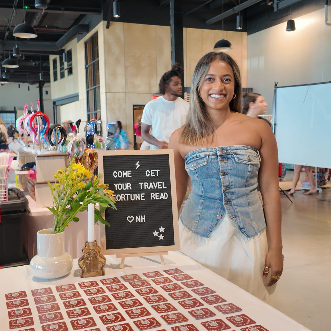 Woman standing behind a table with a 'travel fortune teller' setup in a casual indoor setting.