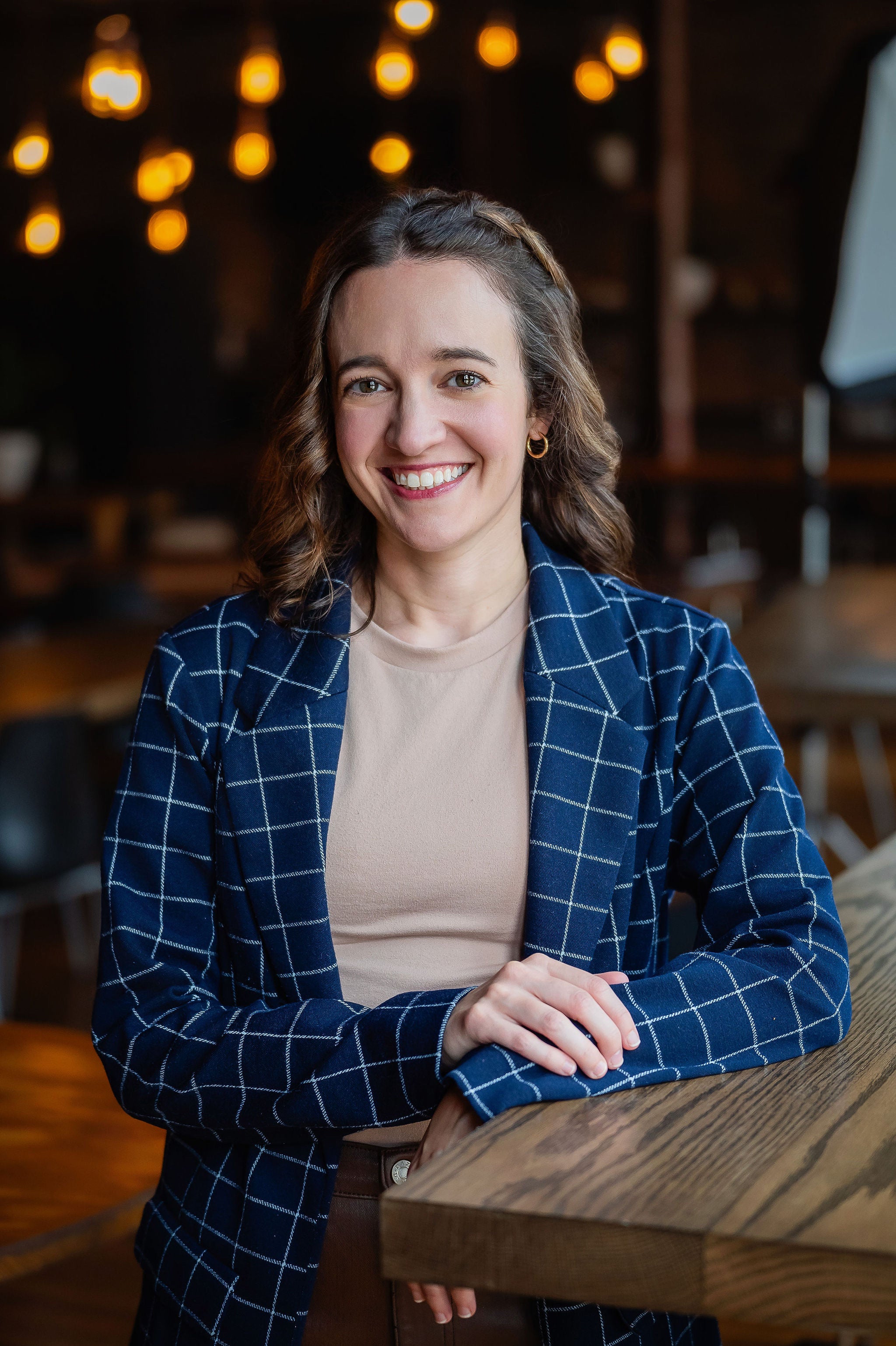 Woman in a blue checkered blazer standing in a warmly lit indoor setting