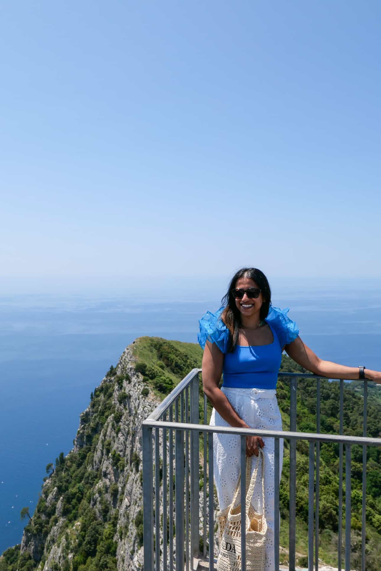 Woman in a blue dress standing on a cliff overlooking the ocean.