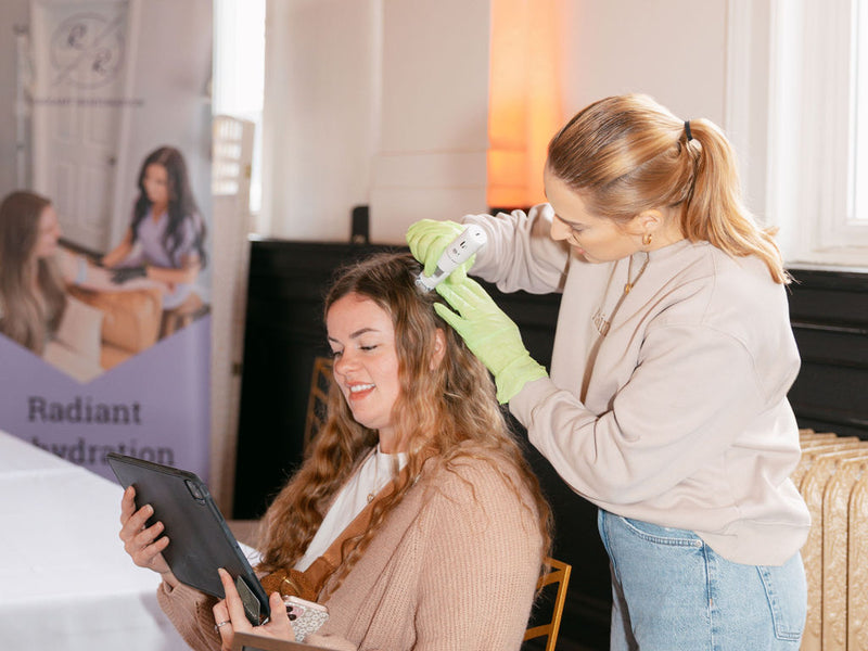 Woman getting her hair styled by another woman at a table with various items.