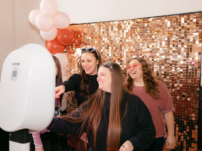 People taking photos with a selfie mirror in front of a glittery backdrop