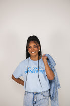 Woman wearing a light blue t-shirt with text, holding a denim jacket against a plain background