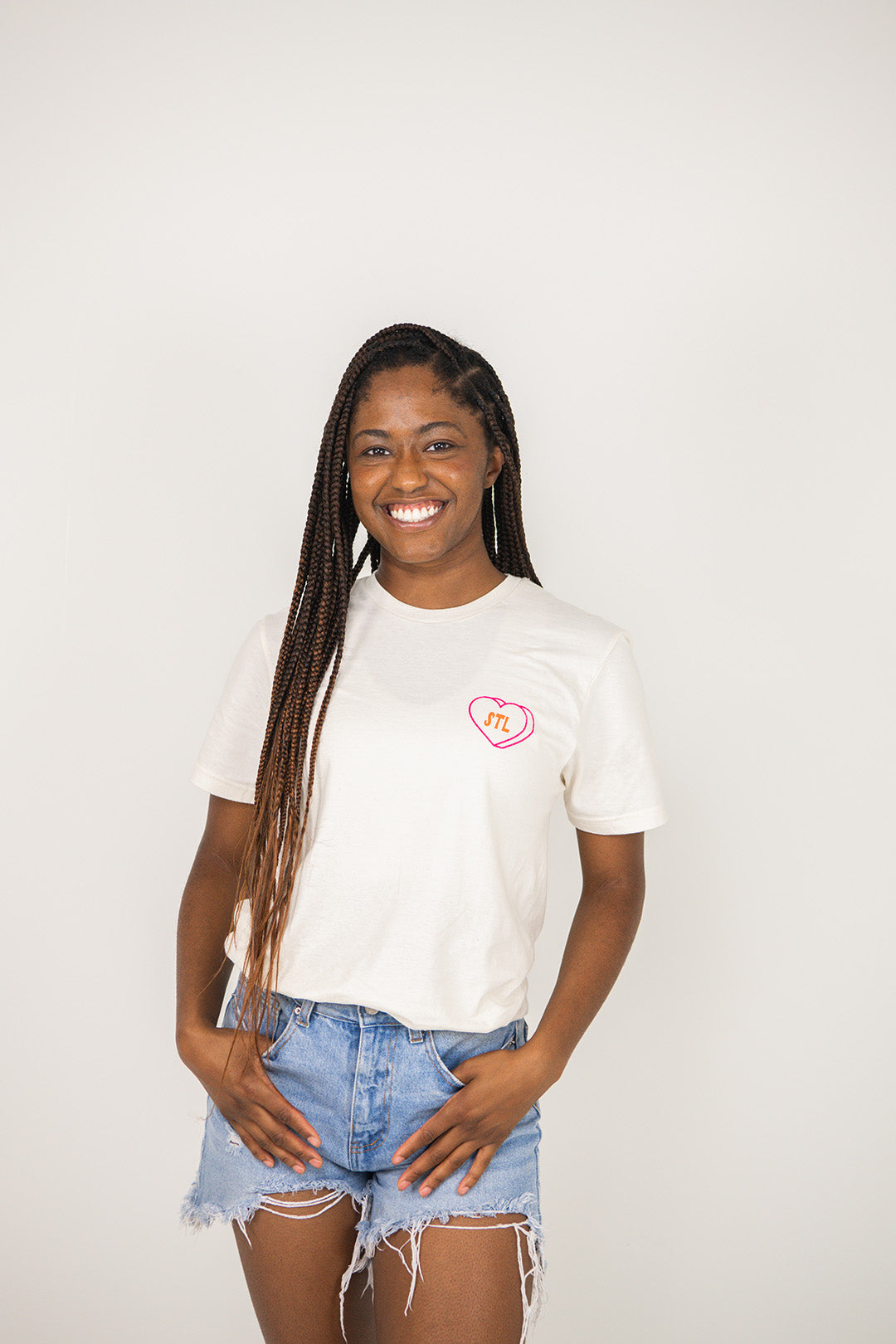 Woman wearing a beige t-shirt with a STL heart design on a plain background