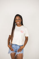 Woman wearing a beige t-shirt with a STL heart design on a plain background