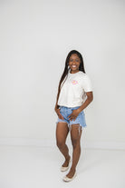 Woman wearing a beige t-shirt and denim shorts on a plain background