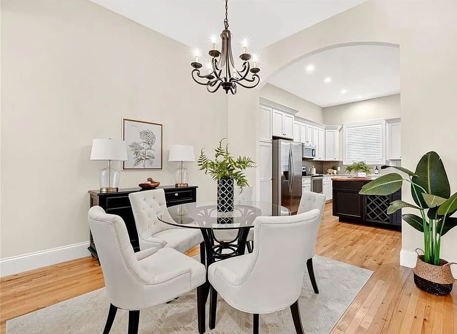 Modern dining room with white chairs, glass table, and kitchen in the background.