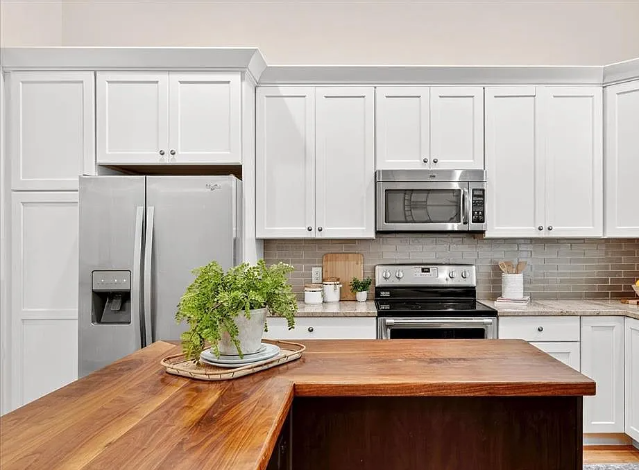 Modern kitchen with wooden island, stainless steel appliances, and white cabinets.