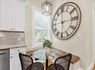 Kitchen with a large wall clock, dining table, and chairs.