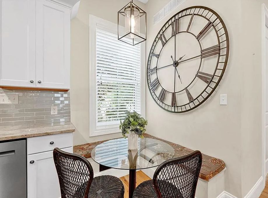 Kitchen with a large wall clock, dining table, and chairs.