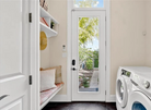 Laundry room with a bench, washer, dryer, and a glass door leading outside.