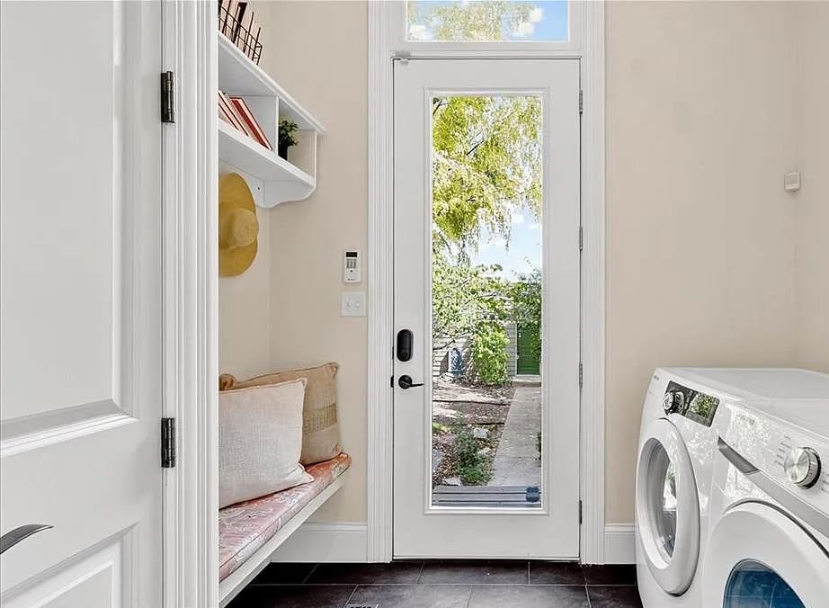 Laundry room with a bench, washer, dryer, and a glass door leading outside.