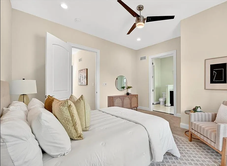 Neatly made bed in a bedroom with a mirror, lamp, and chair.