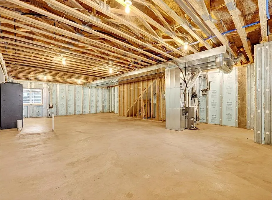 Basement with unfinished wooden ceiling and floor, exposed pipes, and concrete walls.