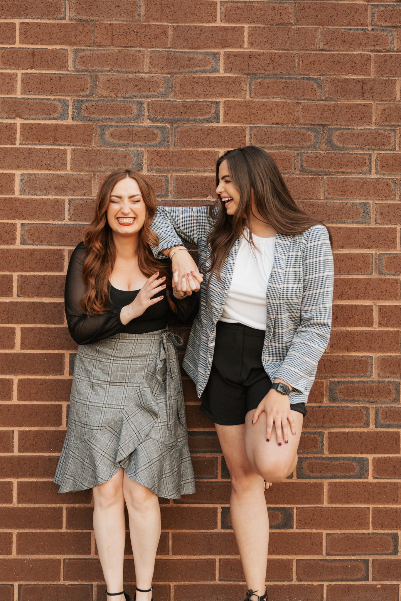Two women standing against a brick wall, smiling and posing for the camera.