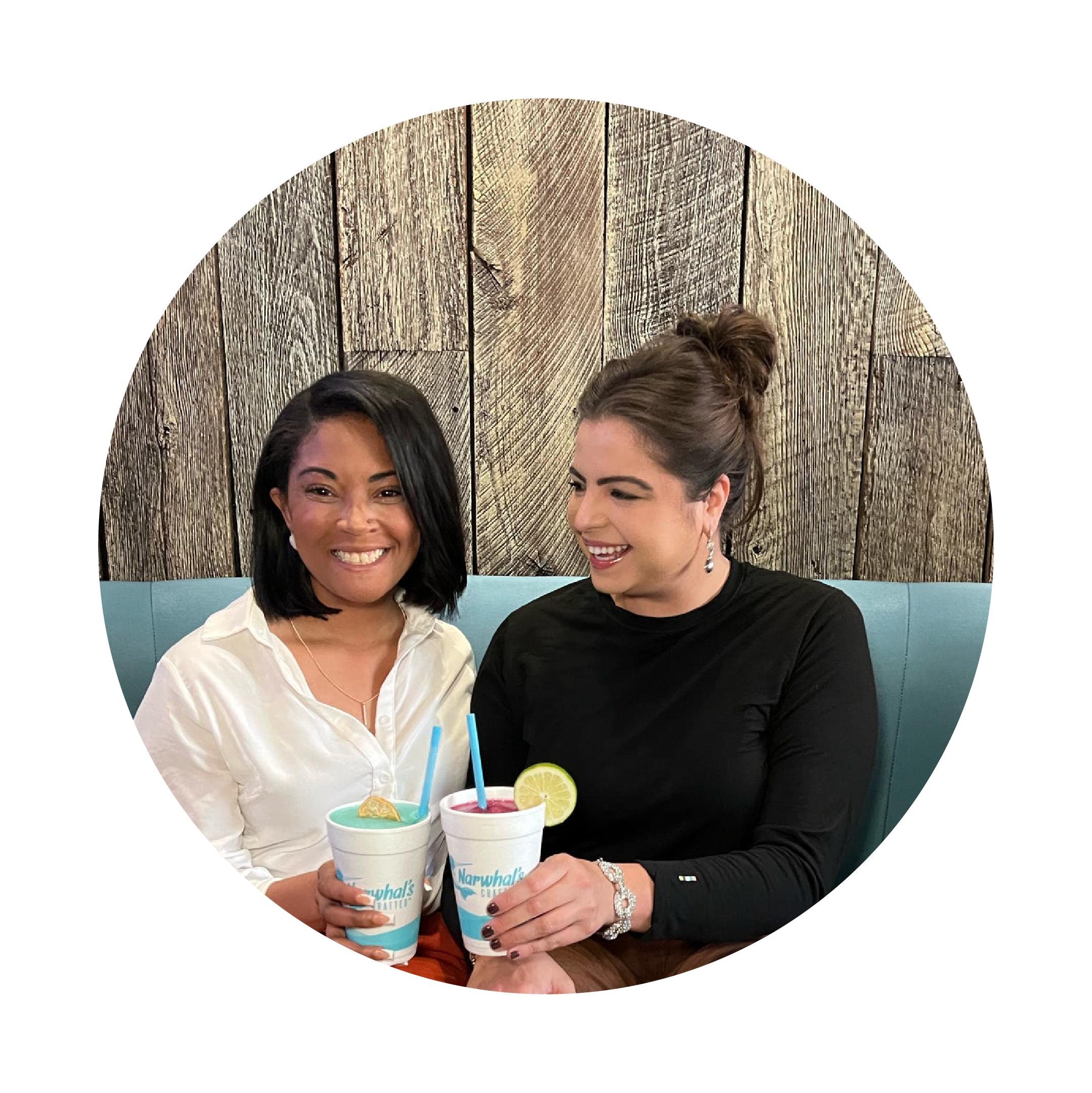Two women sitting together holding drinks with a wooden panel background